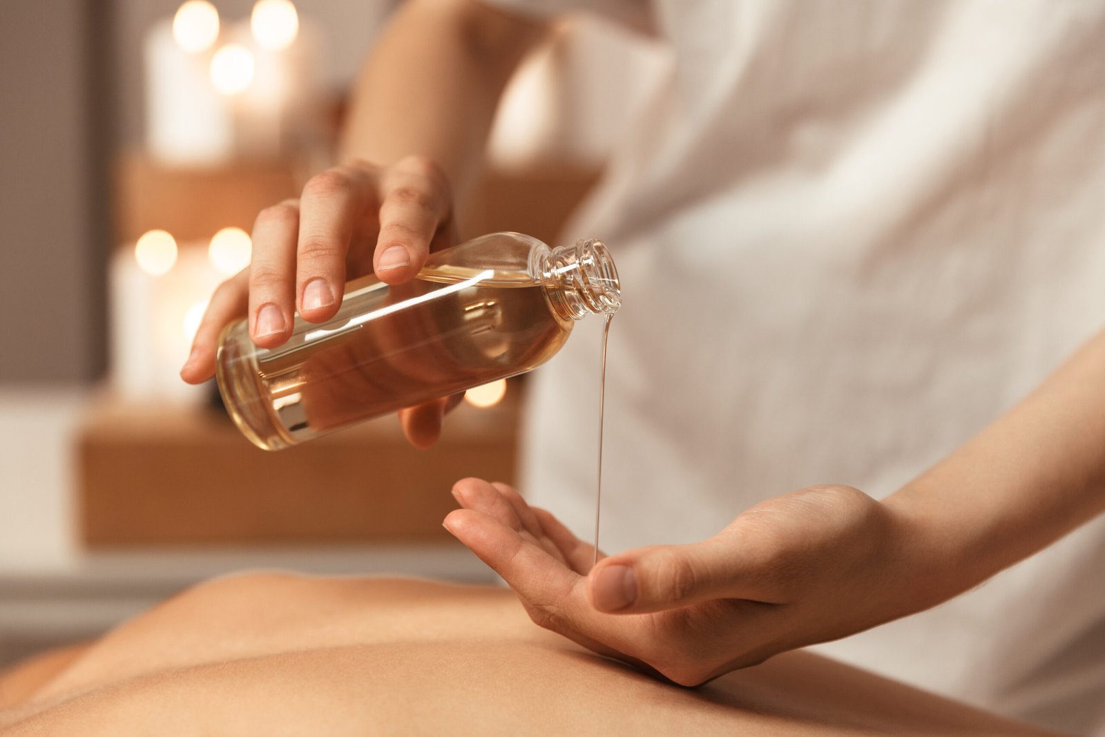 Close up of a woman masseur pouring massage oil on clients back at spa center